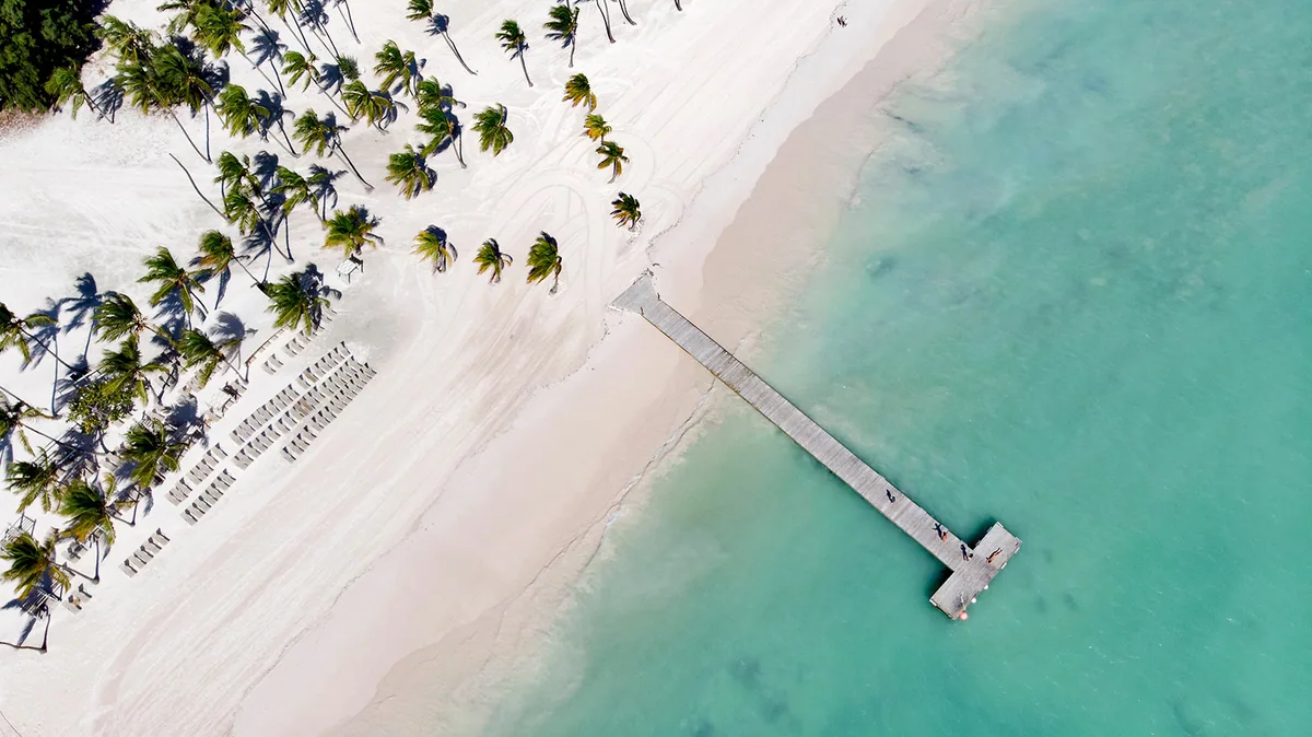 Juanillo from directly above: palms, white sand and a long wooden pier