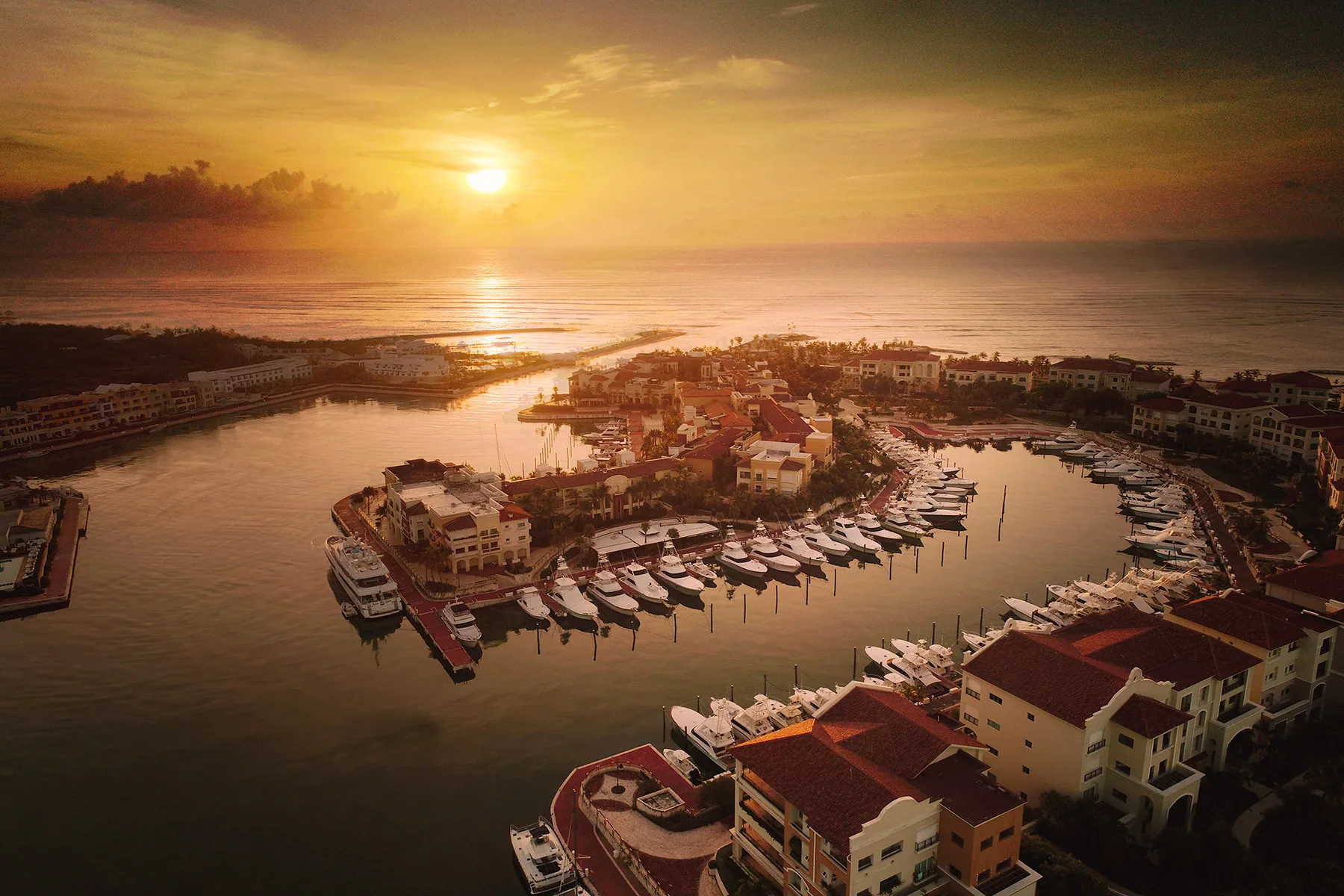 The Marina at Cap Cana from the air at dawn, its quays and moored yachts lit gold by the rising sun