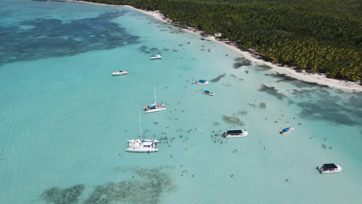Clear turquoise shallows from the air, boats at anchor over the sand